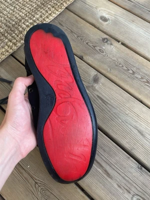 Christian Louboutin skor  - Snygga svarta Christian Louboutin med den klassiska och unika röda sulan. Skorna har svarta skosnören, metallöljetter och en ovandel i textil. Insidan är beige och de har en enkel, stilren look som passar till det mesta. Skorna är lite stora 44or skulle nog säga att det passar uppåt storlekarna 44,5-45