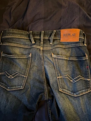Blå Replay jeans med kontrastsömmar - Snygga blå jeans från Replay med klassisk femficksdesign och tydliga kontrastsömmar på bakfickorna. Jeansen har en läderpatch med Replay-logga i midjan och är tillverkade i denim. Perfekta för en avslappnad och trendig look.
