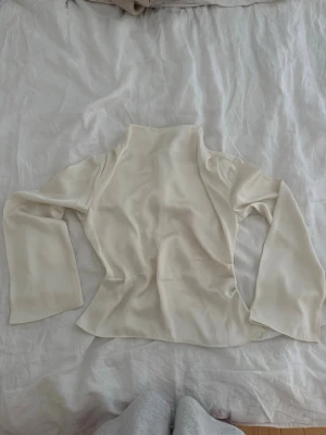 Krämvit blus med hög krage - Säljer en stilren krämvit blus med hög krage och långa ärmar. Blusen har en lätt utsvängd passform och är tillverkad i ett mjukt, slätt tyg som ger en elegant känsla. Perfekt att styla med jeans eller kjol för en trendig look.