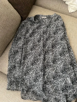 Svartvit zebramönstrad blus Camaïeu - Snygg svartvit blus från Camaïeu med zebramönster. Blusen har lång ärm och en lös, flowy passform. Perfekt för dig som gillar djurmönster och vill sticka ut lite extra. Tunn och lätt i materialet.