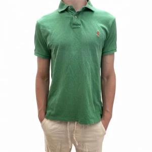 Ralph Lauren piké - Säljer en klassisk grön pikétröja från Polo Ralph Lauren i storlek M. Tröjan har korta ärmar, krage och knappar framtill samt den ikoniska röda loggan broderad på bröstet. Perfekt för en stilren och avslappnad look. Modellen är 183 cm och nypriset är cirka 1200 kr.