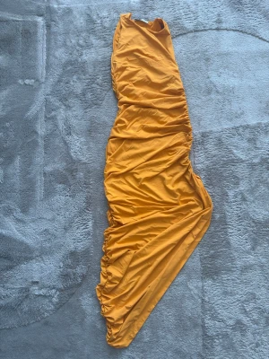 Gul klänning från Zara i S - Snygg gul klänning från Zara i storlek S. Klänningen har en cool draperad effekt längs sidorna och är tillverkad i ett mjukt och lätt material som känns skönt mot huden. Perfekt för dig som vill sticka ut med färg och stil.
