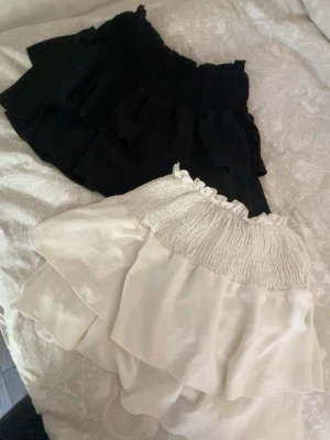 Svart och vit volangkjol - båda för 100kr, en för 75kr ! Två korta kjolar i svart och vitt med volangdetaljer och smockad midja. Perfekta för en trendig och avslappnad look. Kjolarna har en luftig känsla och passar bra till varma dagar.