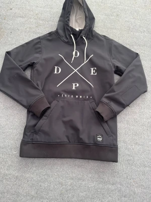 Svart hoodiejacka - Svart hoodiejacka från Dope med vit grafisk logga på bröstet. Jackan har huva med vita dragsnören, stor magficka och ribbade muddar. Insidan är fodrad med mjuk grå fleece för extra komfort. Perfekt för dig som gillar streetwear och snygga detaljer.
