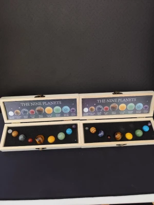 2 st Planetset i träask med stenar - Snyggt set med nio planeter i form av färgade stenar, levereras i två ljusa träaskar med svart skumgummi och plansch med planetnamn. Perfekt som dekoration eller present till rymdintresserade. Varje planet har unik färg och mönster.