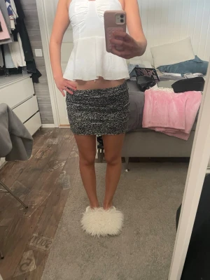 Svartvit kortkjol - Säljer en svartvit kortkjol med melerat mönster. Kjolen är figurnära och stickad, vilket ger en skön och trendig look. Perfekt att matcha med en enkel topp för en snygg outfit.
