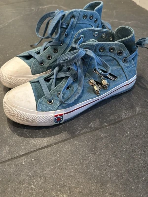 Blå denim high top sneakers - Snygga blå sneakers i denim med högt skaft och vita gummidetaljer. Dragkedja på sidan och coola metalldetaljer. Knyt snöre både på fram och baksida vilket gör skon unik. Perfekt för sommar sneaker och är jätte bekväma.