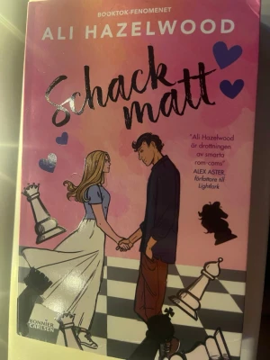 Schackmatt av Ali Hazelwood - En romantisk ungdomsroman av Ali Hazelwood med färgstarkt omslag i rosa och lila toner. Boken handlar om Mallory och schackvärlden, med illustrationer av schackpjäser och två unga personer på framsidan. Perfekt för dig som gillar smarta rom-coms och spännande tävlingar.