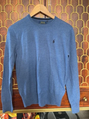 Blå tröja från Polo Ralph Lauren - Snygg blå tröja från Polo Ralph Lauren med rund halsringning och diskret broderad logga på bröstet. Tillverkad i mjukt och tunt material som passar perfekt till lager på lager. Klassisk och stilren design med ribbade muddar vid ärmslut och nederkant.
