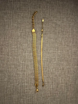 Två guldiga armband i metall - Två stilrena armband i guldig metall. Det ena har ett brett, nätliknande mönster och justerbar kedja, medan det andra är smalare och slätt. Perfekta för att ge en elegant touch till din outfit.