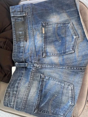 Lågmidjade jeansshorts  - Snygga blå lågmidjade shorts med slitna detaljer. Shortsen har knapp- och dragkedjestängning samt bälteshällor. Midjemått: ca 35, säljer pga de är för stora 