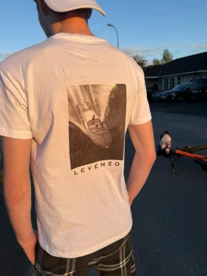 Vit skräddarsydd t shirt från LEVENZO! ✨ - Vit t-shirt från Levenzo med ett stort svartvitt tryck av en båt på ryggen och diskret logga framtill. Klassisk passform och rund hals. Perfekt för dig som gillar stilrena plagg med en twist. En tröja som passar alla tillfällen, en tröja som inte kommer att göra dina förhoppningar missnöjda! Ifall du undrar något, var inte rädd att ställ frågan✨❤️