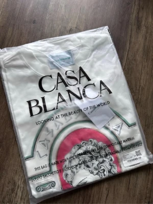 Vit t-shirt från Casablanca - Vit t-shirt från Casablanca med tryck framtill som visar ett klassiskt konstmotiv och texten 'Equipement Sportif 2024'. T-shirten har rund hals och korta ärmar. Perfekt för dig som gillar stilrena plagg med unik design.