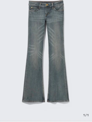 Bootcut jeans från Cheap Monday - Säljer ett par blå bootcut jeans från Cheap Monday med coola slitningar och klassisk femficksdesign. Jeansen har en unik patch med Cheap Mondays ikoniska döskalle på bakfickan. Perfekta för dig som gillar retrovibbar och streetstyle.