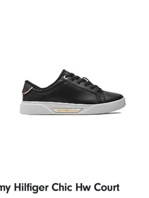 Svarta sneakers från Tommy Hilfiger - Säljer ett par svarta sneakers från Tommy Hilfiger med vita sulor och gulddetalj vid hälen. Skorna har snörning och är tillverkade i skinnliknande material. Perfekta för en stilren och enkel look.