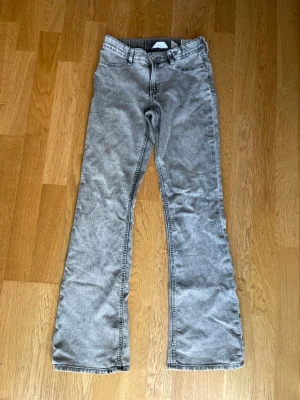 Grå bootcut jeans - Säljer ett par grå bootcut jeans med klassisk femficksdesign och dragkedja med knapp. Jeansen har en lätt tvättad look och är tillverkade i denim. Perfekt för dig som gillar en avslappnad och trendig stil.12-14 år 