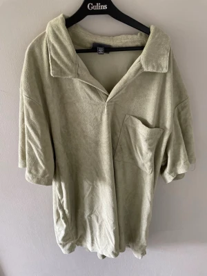 Ljusgrön frotté t-shirt med krage från H&M - T-shirt i ljusgrön frotté med avslappnad passform, stor bröstficka och bred krage. Modellen är loose och har korta ärmar, perfekt för en chill och trendig look.