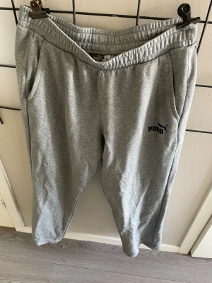 Grå mjukisbyxor från Puma XL - Snygga grå mjukisbyxor från Puma med elastisk midja och två sidofickor. Byxorna har en avslappnad passform och Puma-logga tryckt på vänster ben. Tillverkade i mjukt bomullsmaterial som är skönt mot huden.