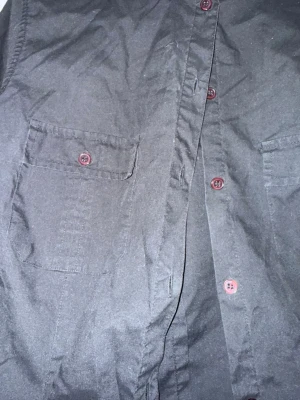 Svart skjorta  - Svart skjorta från Lindex. Står att det är storlek 44, men passar mig som är en storlek S. Den är i bra skick, en knapp är lite lös, men inget som påverkar eller att sy fast hårdare. 