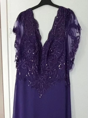 Lila långklänning med spetsdetaljer - Elegant lila långklänning med djup v-ringning och vackra spetsdetaljer upptill. Klänningen har transparenta, korta ärmar i chiffong och skimrande paljetter som ger extra effekt. Perfekt för dig som vill sticka ut med en unik look.                                          https://www.jjshouse.com/se/product/a-linjeklaenning-skopa-illusion-ankel-lang-spets-chiffong-cocktailklaenning-med-paljetter-016251348-g251348