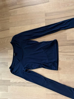 Mörkblå långärmad topp Gina Tricot - En stilren mörkblå långärmad topp från Gina Tricot. Toppen har rund halsringning och är figurnära i modellen. Perfekt att matcha med jeans eller kjol för en enkel och snygg look.