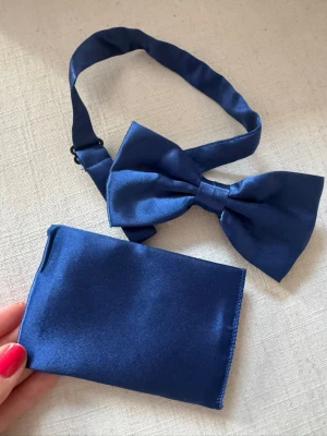 Marinblå fluga och näsduk i satin - Säljer en stilren marinblå fluga med matchande näsduk i glansigt satintyg. Perfekt accessoar för att lyfta din outfit med en elegant touch. Flugan har justerbart band och näsduken är fyrkantig.