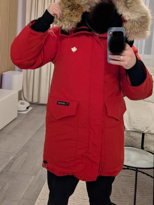 Röd parkas från Canada Goose - Säljer en röd Canada Goose Heli Arctic parka med en stor och fluffig päls.Jackan har flera fickor, reflexdetalj på ryggen och klassiska Canada Goose-loggan på ärmen. Perfekt för kalla vinterdagar och riktigt snygg streetstil. Detta är en av Canada Goose varmaste jackor. Storlek: 2xs, passar en kille som bär S och tjej som bär M. Priset är fast, billigare nu vid slutet av vintern. Kom och fynda!