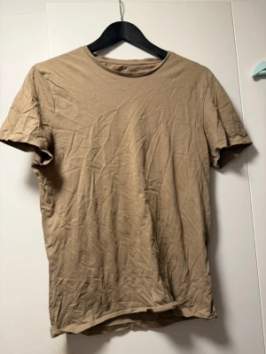 Beige basic t-shirt i bomull - En enkel beige t-shirt med rund hals och korta ärmar. Tillverkad i mjuk bomull och har en normal passform. Perfekt att matcha med jeans eller shorts för en clean och avslappnad stil.