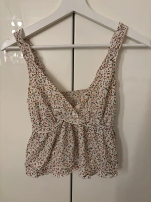 Somrig topp - Söt blommig linnetopp med omlott-design och breda axelband. Toppen har smockad rygg och volangdetaljer längs nederkant och axelband. Så fin på sommaren, i strl xs men stretchig så en xs-m