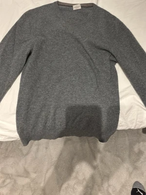Grå stickad tröja från Rose & Born - Snygg grå stickad tröja från Rose & Born med rund halsringning och ribbade muddar. Tillverkad i mjukt material som känns lyxigt och passar perfekt till lager på lager. Enkel och stilren design som funkar till många olika looks.