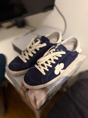 The gallerist skor blå nypris 2700* helt nya! - The Gallerist skor blå storlek 46, jag har 44 och den passar mig. Har dock aldrig använt den utomhus de är alltså helt nya. Så storleken är bra för folk som har 44/45 oxå den sitter på foten bra.                                                                                 sneakers i mörkblå mocka med vit blomdetalj på sidan och vita skosnören. Klassisk låg modell med robust sula och broderad logga på plösen. Perfekta för dig som gillar streetwear och unika samarbeten. 