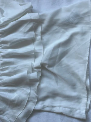 Vit blus i sidenlook - Säljer en vit blus med volangdetaljer och en lyxig sidenkänsla. Blusen har en lös passform, perfekta för sommarens varma dagar. Materialet ger en mjuk och glansig finish som känns riktigt fräsch.