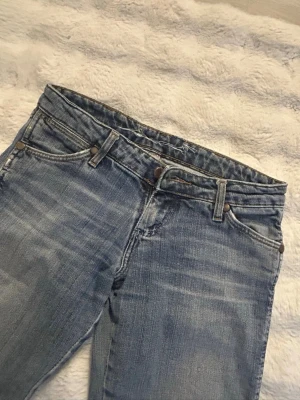 Wrangler jeans - Ett par ljusblå bootcut low waist jeans med slitningar, inte andvända mycket och i bra skick! Står storlek 26-32 men skulle kunna tänka mig att de passar mindre storlekar då de passar mig som har det! 💕
