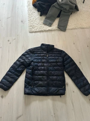 Ralph lauren jacka  - Snygg svart dunjacka med quiltad design och dragkedja framtill. Jackan har två fickor med dragkedja och hög krage som skyddar mot vind. Perfekt för kalla vinterdagar och enkel att matcha med olika outfits. Smått hål man ser på sista bilden