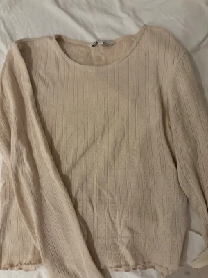 Beige ribbad långärmad topp - Snygg beige långärmad topp med ribbad struktur och diskret mönster. Rund halsringning och lätt vågig kant nedtill ger en söt touch. Jätte gulligt att ha till fina mjukis eller pyjamas byxor funkar även för en vardaglig look med jeans 
