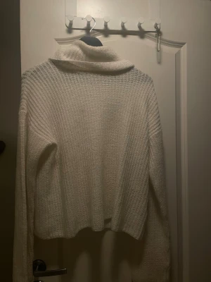 Vit stickad polotröja - Mysig vit stickad polotröja med avslappnad passform och långa ärmar. Tröjan har en bred polokrage och är ribbstickad för extra struktur. Perfekt för kalla dagar och enkel att matcha med olika outfits.