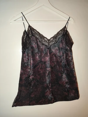 Mörk sammetslinnetopp med spets ZARA - Säljer en mörk, mönstrad linnetopp i sammet med tunna axelband och vacker svart spets längs urringningen och kanterna. Toppen har en mjuk, glansig yta i svart och vinröda toner och ger en riktigt elegant känsla.