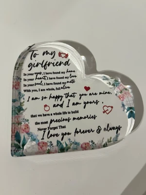 Dekorativt hjärta med kärleksbudskap - Dekorativt hjärta i genomskinlig akryl med tryckt text 'To my girlfriend' och romantiskt budskap. Blommönster i rosa och grönt längs kanterna samt små röda hjärtan och ringar. Perfekt som personlig present eller dekoration.