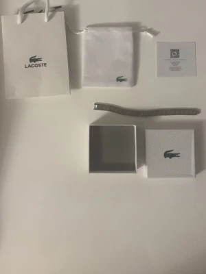 Silverfärgat armband från Lacoste - Stilrent armband från Lacoste i silverfärg med klassisk länkdesign. Kommer med originalförpackning, tygpåse och presentpåse med Lacoste-logga. Perfekt accessoar för dig som gillar minimalistisk och tidlös stil.