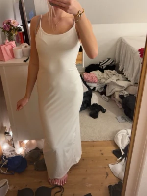 Vit långklänning med smala axelband - Säljer en enkel och stilren vit långklänning med smala axelband och figurnära passform. Klänningen har en rundad urringning och är ärmlös, perfekt för varma dagar eller sommarens tillfällen.