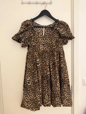 Kort leopardklänning med puffärm - Säljer en kort klänning med leopardmönster och puffiga korta ärmar. Klänningen har en lös passform och rund halsringning. Perfekt för dig som vill sticka ut med ett djurmönster och gillar trendiga detaljer.