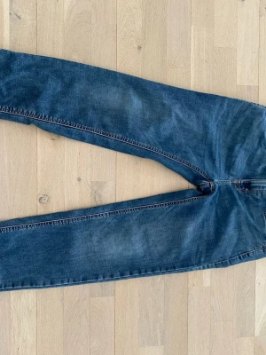 Mörkblå raka jeans - Säljer ett par mörkblå jeans med rak passform och klassisk femficksdesign. Jeansen har subtila slitningar och kontrastsömmar. Perfekta till en avslappnad stil och tillverkade i denim. Märke och storlek är ej angivet.