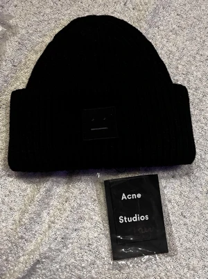 Svart ribbstickad mössa Acne Studios - Säljer en helt ny ribbstickad mössa från Acne Studios med den ikoniska Face-loggan framtill. Mössan är i tjockt, mjukt material och har en bred uppvikt kant. Perfekt för dig som vill ha en stilren och trendig accessoar till hösten och vintern.