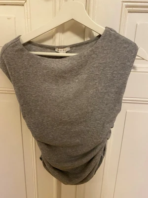 Grå ärmlös topp från Amisu - Snygg grå ärmlös topp från Amisu med draperad effekt i sidan. Tillverkad i mjuk bomullsblandning och har en enkel, stilren design med rund halsringning. Perfekt att matcha med jeans eller kjol för en trendig look. Skulle säga att tröjan massar s/m mer 