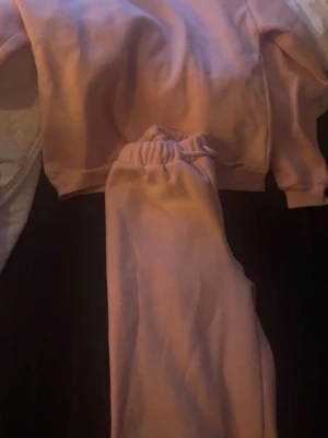 Rosa mjukisset med sweatshirt och byxor - Mysigt loungewear-set i ljusrosa färg med matchande sweatshirt och byxor. Tröjan har rund hals och långa ärmar, byxorna har resår i midjan för extra komfort. Perfekt för chill hemma eller slappa dagar. Materialet känns mjukt och skönt mot huden.