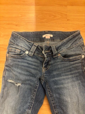 Blå slitna jeans från gina tricot - ALDRIG ANVÄNDA! Säljer ett par blå jeans från gina tricot med slitningar på låret och snygga detaljerade bakfickor. Jeansen har klassisk femficksmodell, normal midja och kontrastsömmar. Perfekta för en avslappnad och trendig look.