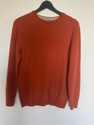 Ulltröja från Lagency - Snygg orange stickad tröja från Lagency i  M. Tröjan har rund halsringning och långa ärmar, perfekt för att hålla värmen under kyliga dagar. Materialet är mjukt och skönt, 100% ull.Enkel och stilren design som funkar till många outfits.
