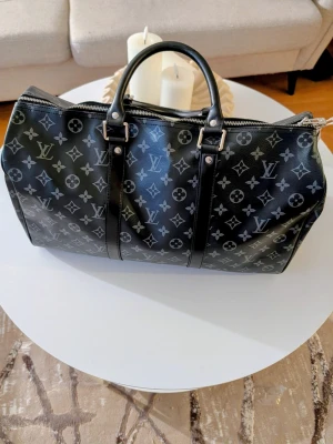 Iouis Vuitton resväska  - Säljer en ikonisk reseväska i en elegant mörkgrå och svart färgkombination med det karaktäristiska mönstret. Detta är den perfekta följeslagaren för både weekendresor och som lyxigt handbagage på flyget.