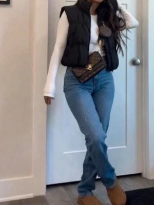 Svart puffig dunväst med hög krage - Snygg svart dunväst med puffig design och hög krage. Västen har dragkedja framtill och två fickor på sidorna. Perfekt att slänga över en hoodie eller långärmad tröja för en chill och trendig look.