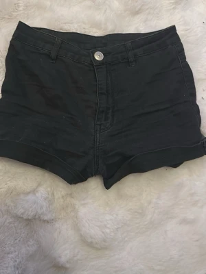 Svarta högmidjade shorts - Snygga svarta shorts med hög midja och klassisk femficksdesign. De har knapp och dragkedja framtill samt korta ben. Perfekta till sommaren och lätta att matcha med olika toppar.
